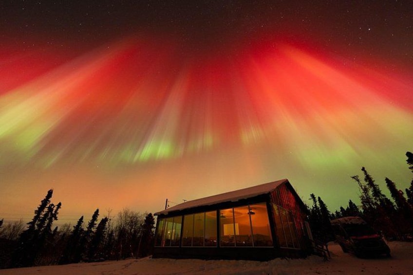 A cabin with a glass facade under a vibrant aurora display. 1
