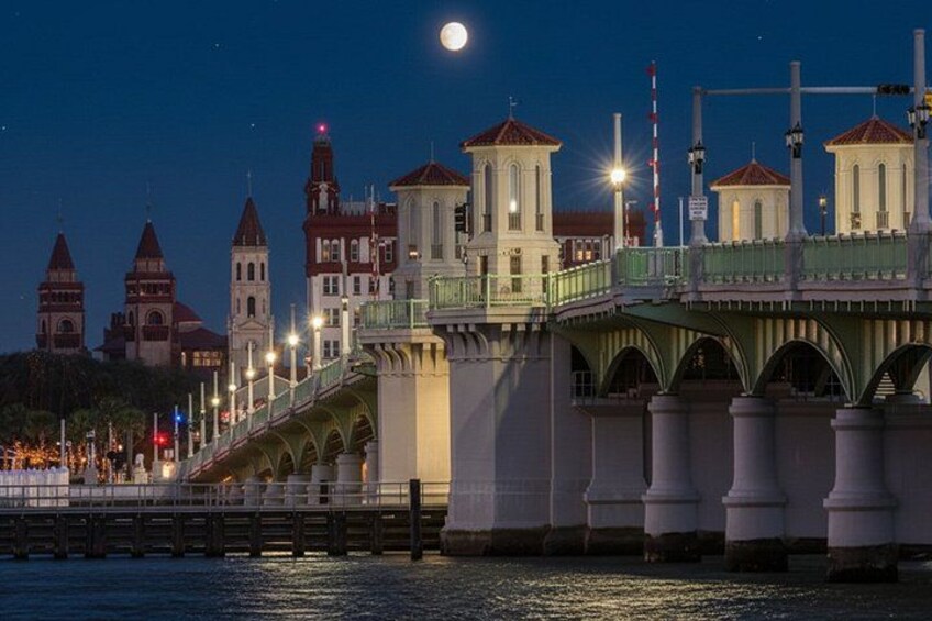 A bridge with a green walkway, a river, and buildings with red roofs in the background. 5