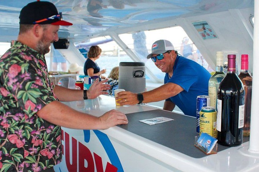 Un bar en un barco con gente interactuando, botellas y latas en la barra. 3