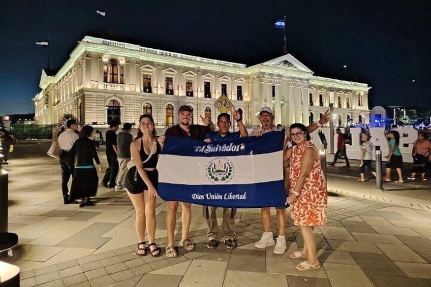 A group of people holding a flag in front of a large white building with columns. 1