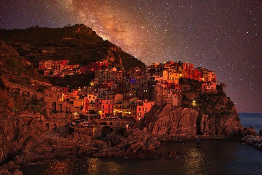 A coastal village at night with illuminated buildings, a rocky shoreline, and a starry sky. 2