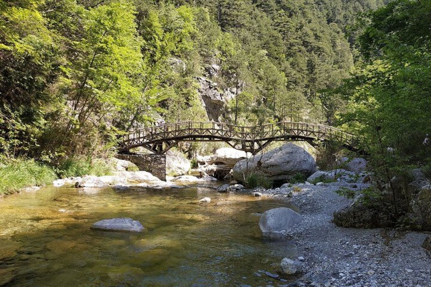 A wooden bridge over a clear stream, surrounded by rocks and lush greenery. 1