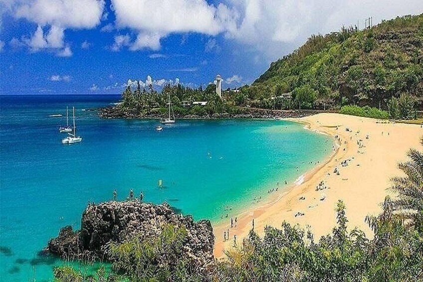 A beach with clear turquoise water, a rocky outcrop, and a small island with buildings in the distance. 1