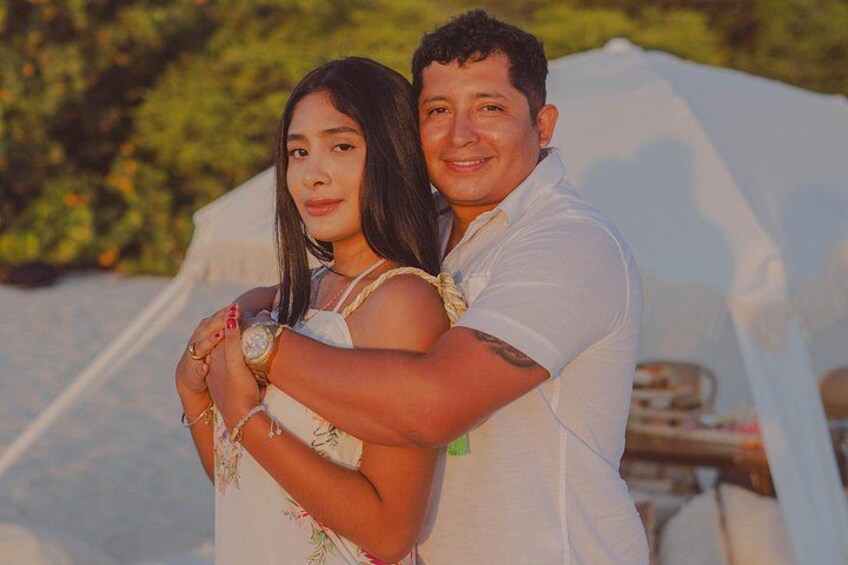 A couple embracing in front of a white tent with greenery in the background. 4