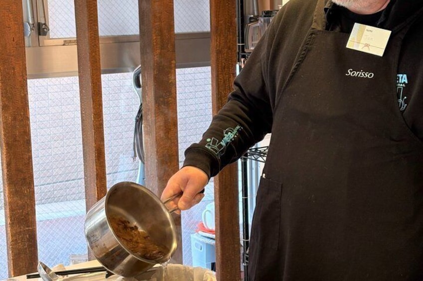 Une personne portant un tablier noir verse le contenu d’une casserole en acier inoxydable. 2