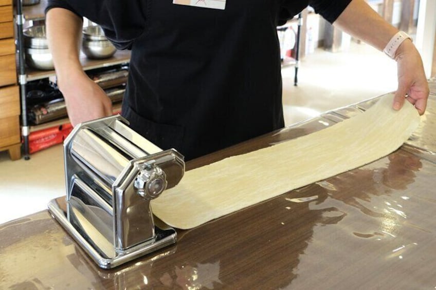 Une personne utilise une machine à pâtes pour abaisser la pâte sur un plan de travail en bois. 5