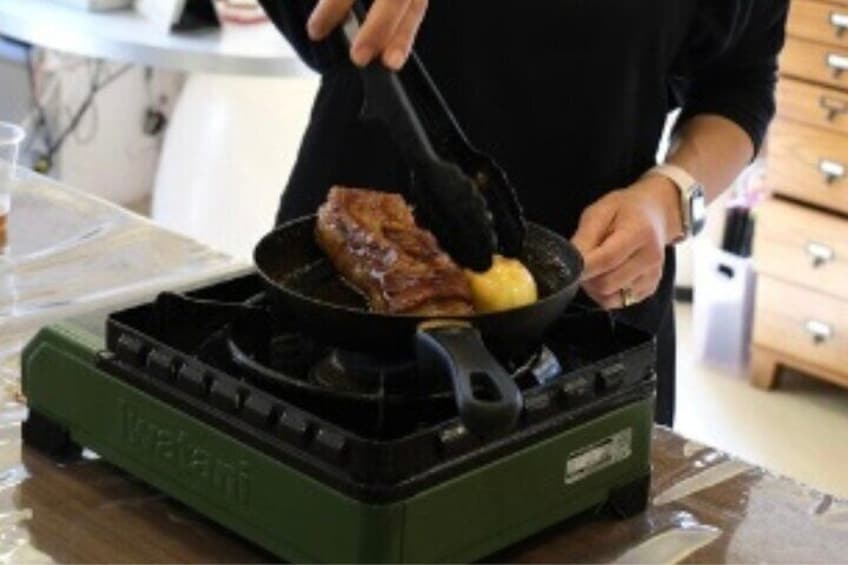 Une personne est en train de cuire un morceau de viande dans une poêle sur un réchaud portatif. 4