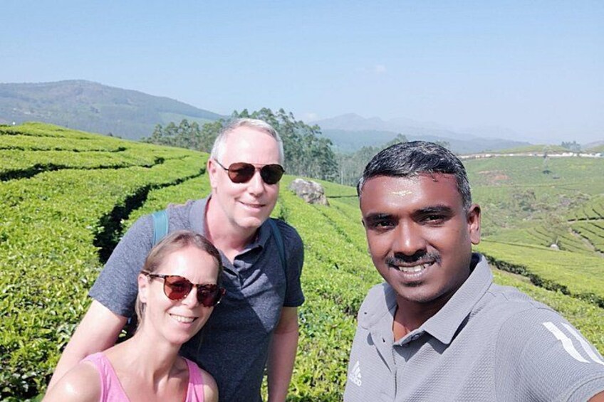 Three people standing in a tea plantation with rows of tea bushes. 4