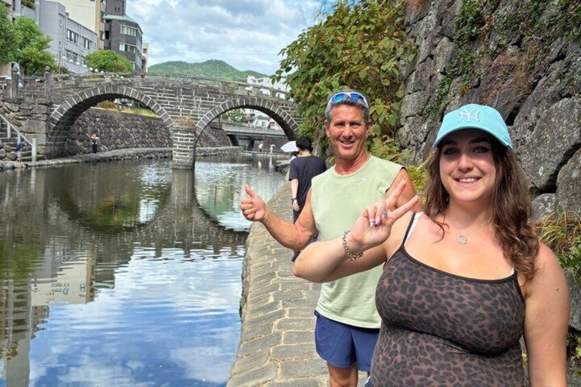 Un pont de pierre enjambant une rivière paisible, une personne portant un haut à motifs léopard et une autre vêtue d’une chemise verte. 3