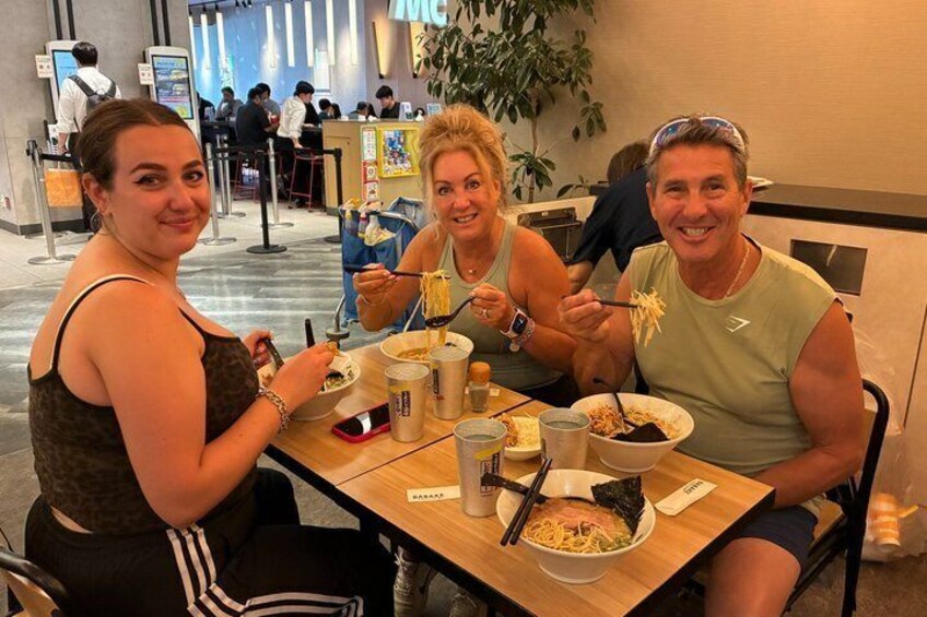 Trois personnes sont attablées dans un restaurant, devant une table en bois, avec des bols remplis de nourriture et divers condiments. 5