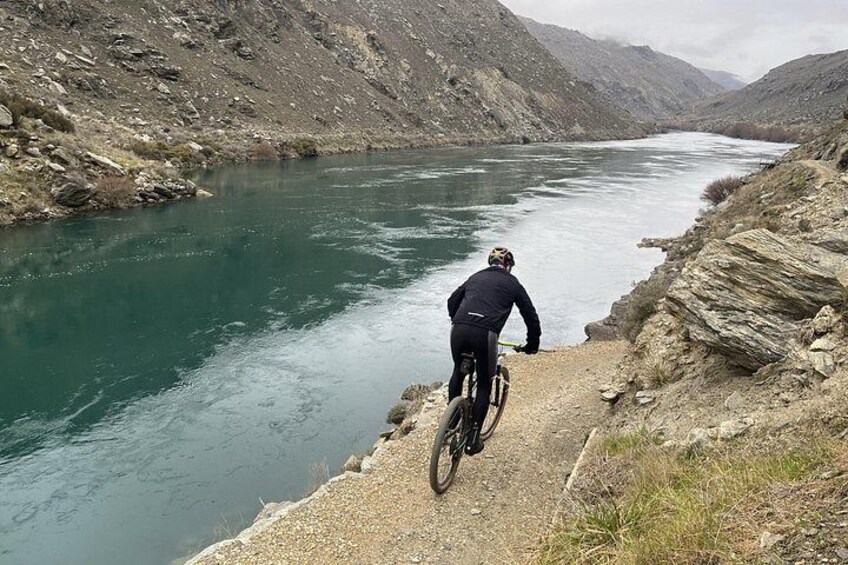 A person riding a mountain bike along a river trail in a mountainous area. 4