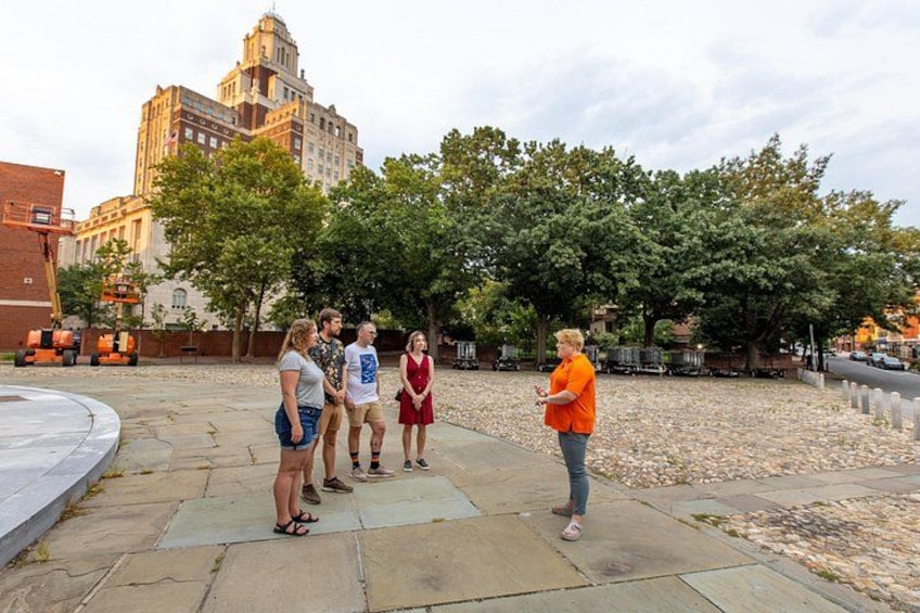 A group of people standing on a paved area with trees and a large building in the background. 3