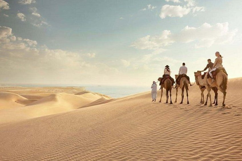 A group of people riding camels across a desert landscape with sand dunes and a clear sky. 2