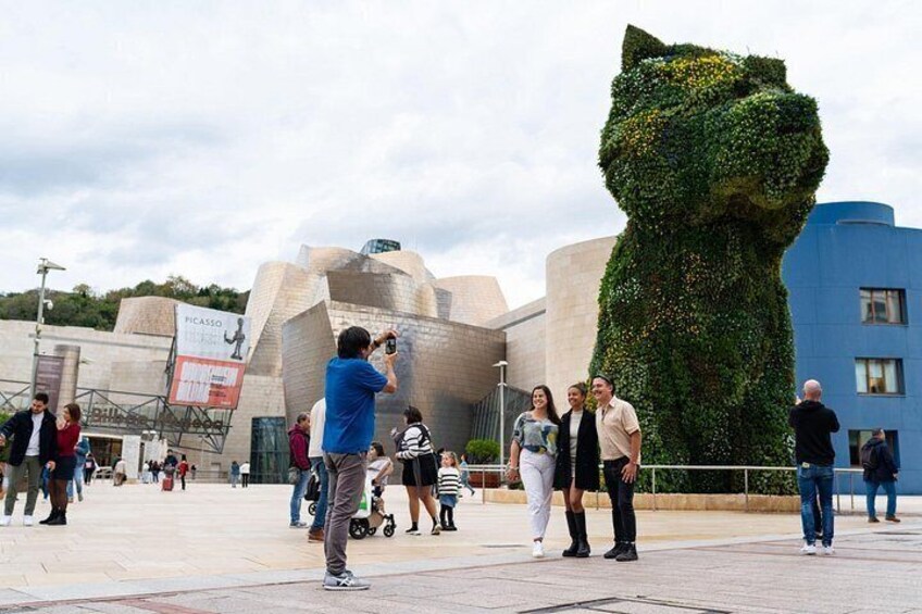 Eine Katzenstatue, ein modernes Gebäude und Passanten auf einem Platz. 2