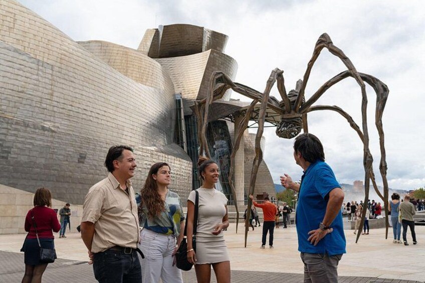 A modern building with a large metallic sculpture of a spider in front of it. 1