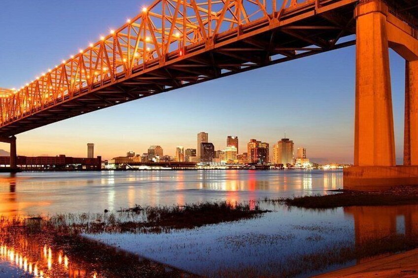 Un puente con luces reflejándose en el agua, una silueta urbana al fondo y un cielo despejado. 3