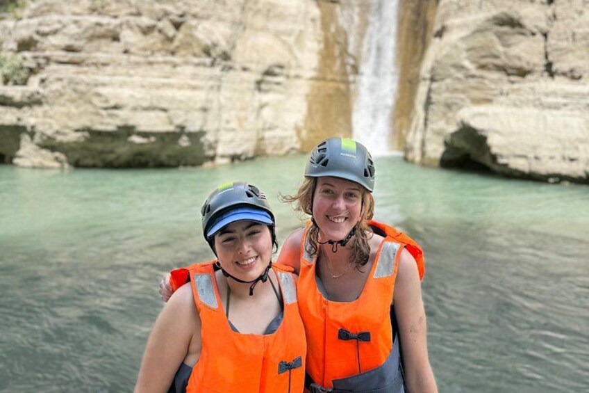 Two people wearing helmets and life jackets near a waterfall. 1