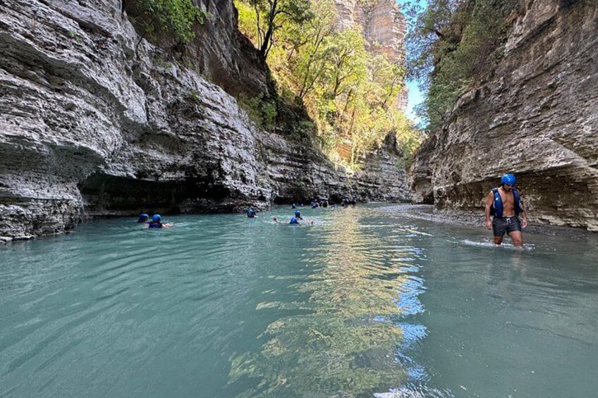 A canyon with water, people in kayaks, and a person standing on the riverbank. 4