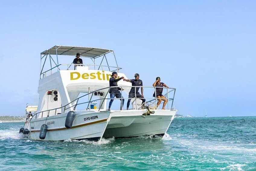 Ein Boot namens 'Destini' mit Personen an Deck, das sich durch türkisfarbenes Wasser bewegt. 1
