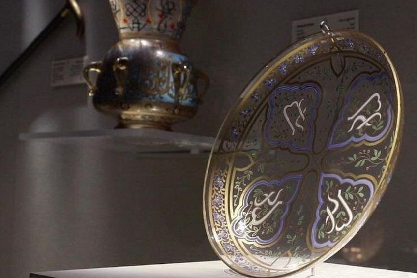 Un plato decorativo con diseños intrincados y un jarrón al fondo. 2