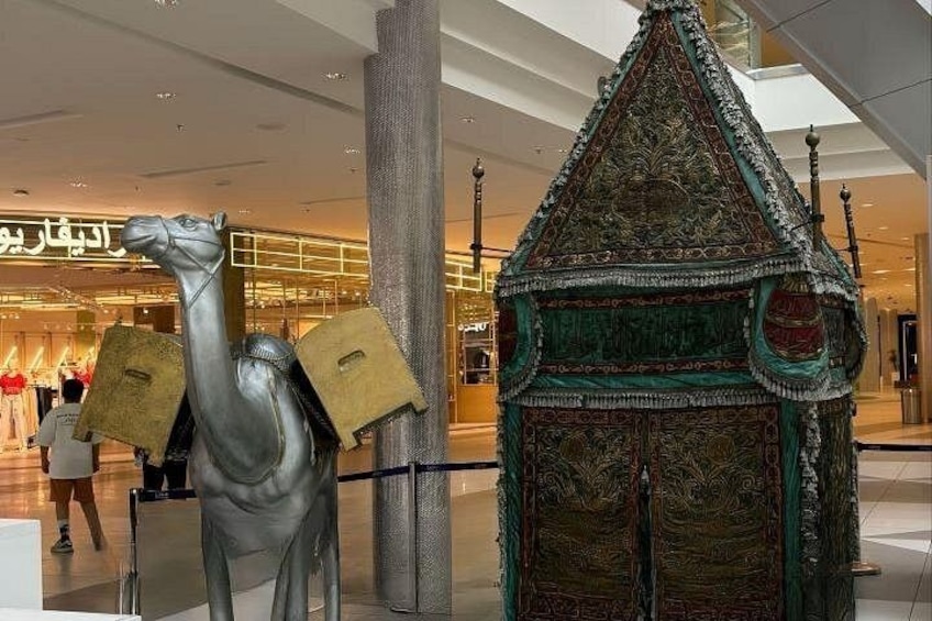 Una escultura de camello con un edificio tradicional y un centro comercial al fondo. 1