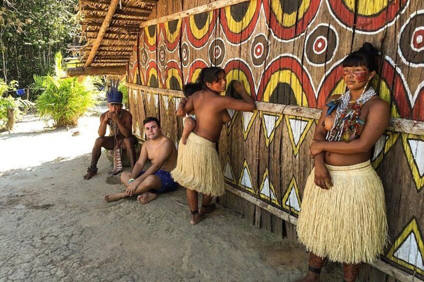 A group of people in traditional attire sitting and standing near a decorated hut. 4