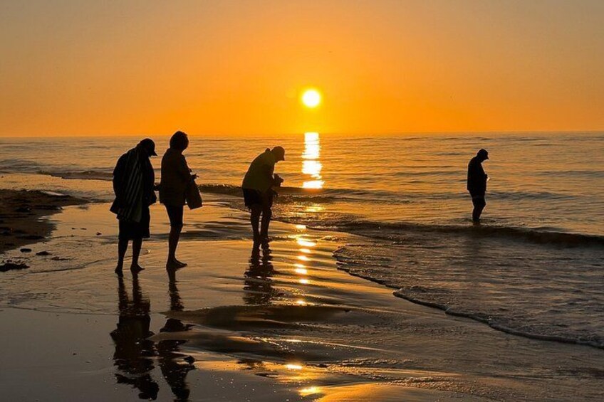Un coucher de soleil sur une plage, avec des personnes debout et se promenant le long du rivage. 1