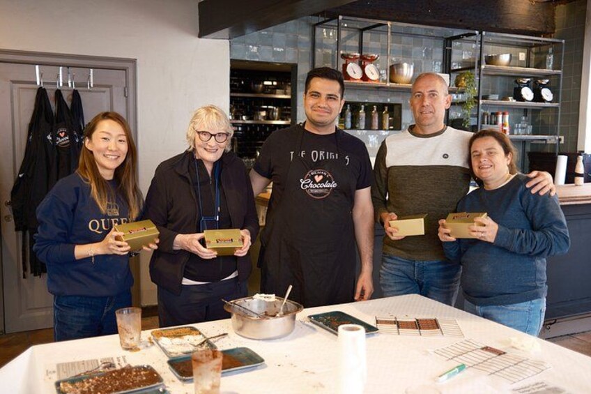 Un grupo de personas sosteniendo cajas en una mesa, con varios objetos y una cocina al fondo. 1