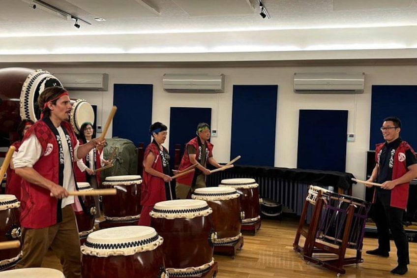 A group of people playing drums in a room with blue acoustic panels. 2