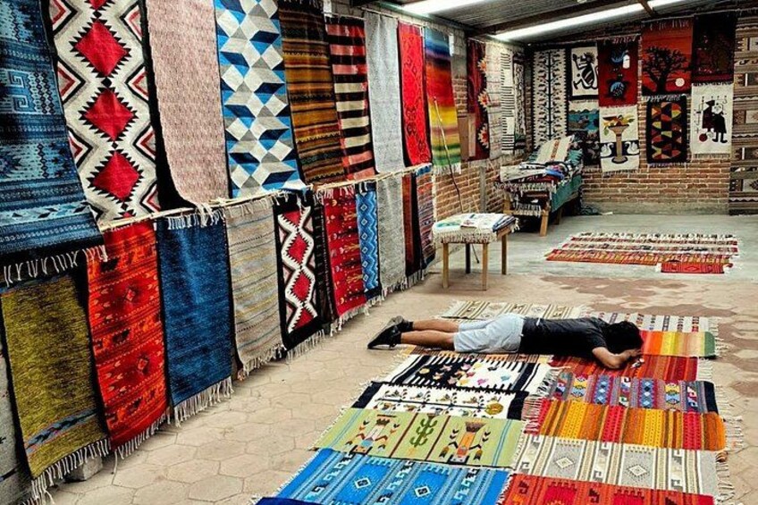 A person lying on a rug in a room with walls lined with various colorful rugs. 1
