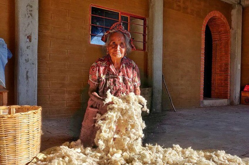 An elderly person processing wool in a rustic building with brick walls and a red archway. 5