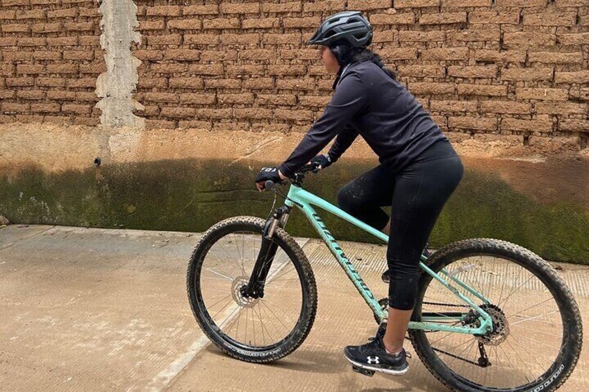 A person riding a teal mountain bike on a concrete path with a brick wall in the background. 3