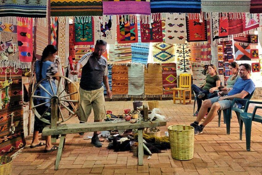 A market stall with colorful textiles, a spinning wheel, and people interacting. 3