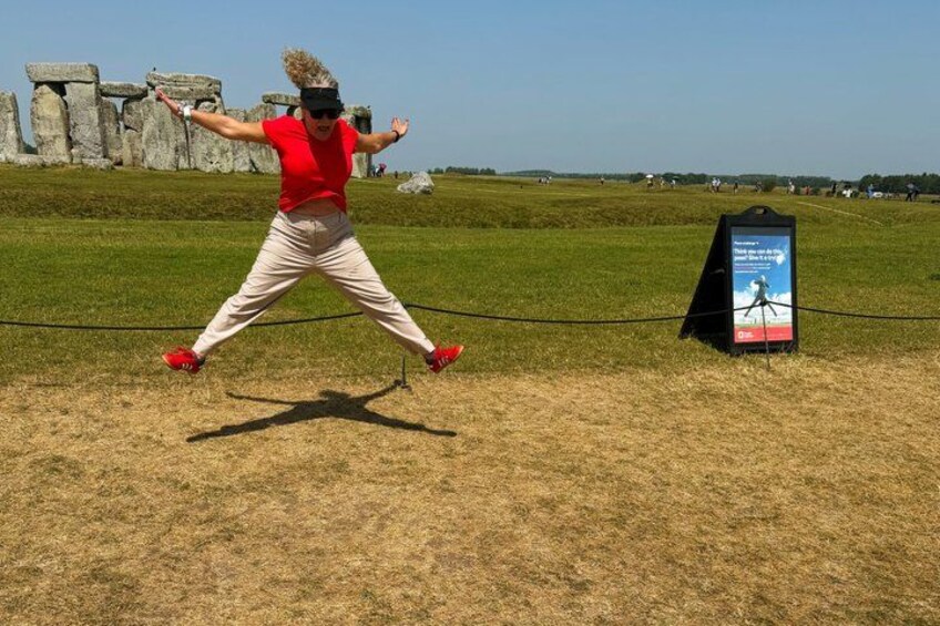 Una persona saltando frente a Stonehenge, con un cartel en el fondo. 2