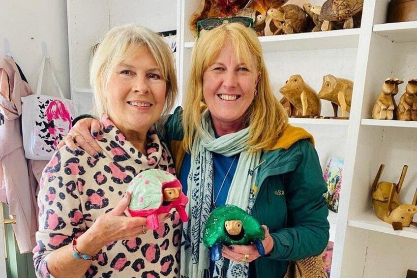 Two people holding plush toys in a room with shelves of wooden animal figurines. 5