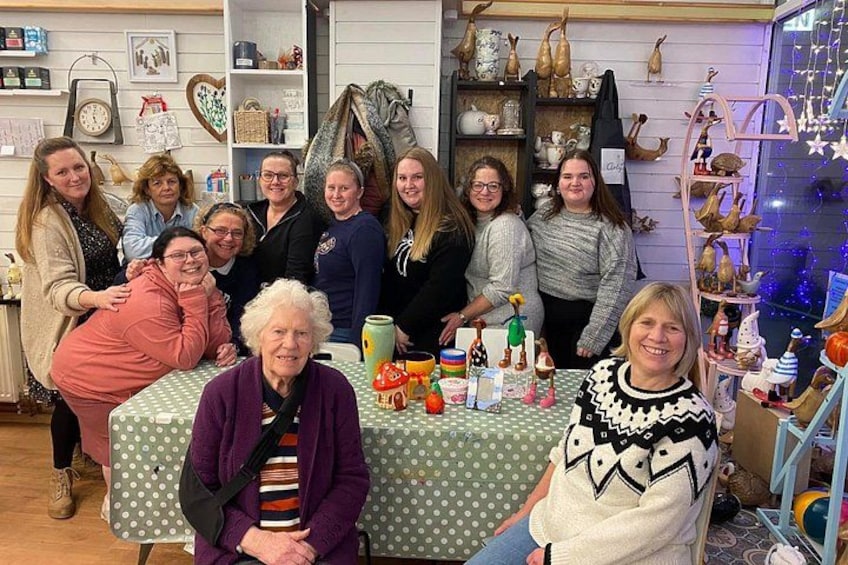 A group of people gathered around a table with various items on it, in a room with shelves and decorative items. 2
