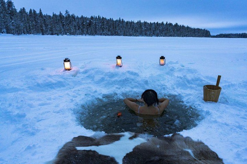 A person relaxing in a snow hole with lanterns and a bucket. 2