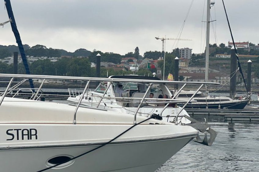 Een witte boot met de naam 'STAR' afgemeerd in een jachthaven, met andere boten op de achtergrond en een stadsbeeld aan de overkant van het water. 3