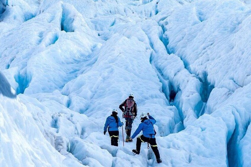 A group of people hiking through a snow-covered glacier with crevasses. 5