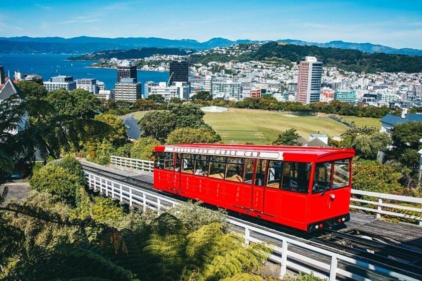 A red cable car on a track with a cityscape in the background. 2