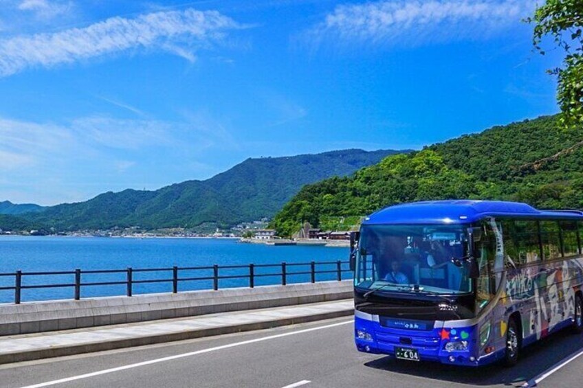 A blue bus driving on a road with a coastal landscape and mountains in the background. 1
