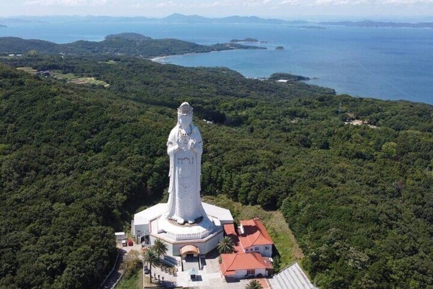 A white statue on a hill with a red-roofed building nearby. 3