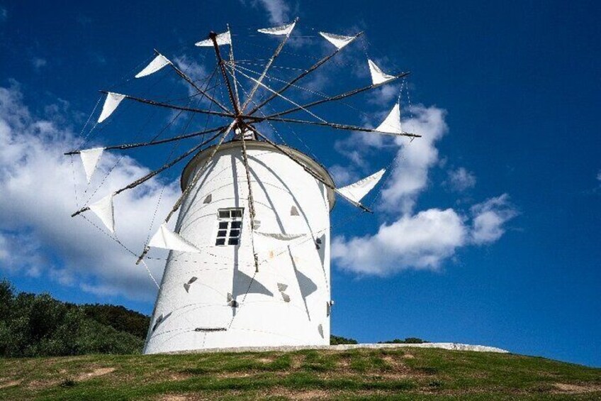 A white windmill with a large sail on a hill under a clear blue sky. 5