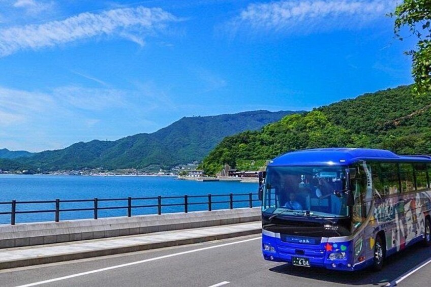 A blue bus driving on a road with a coastal landscape and mountains in the background. 1