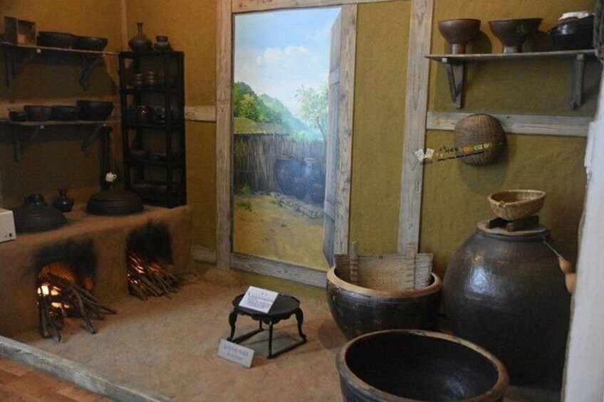 A historical exhibit with pottery, a fireplace, and a painting of a rural scene. 4
