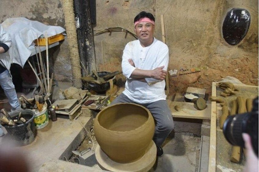 A person sitting in a pottery workshop with clay pots and tools. 5