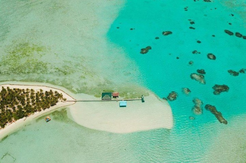 An aerial view of a turquoise lagoon with a small island, a beach, and a boat. 1