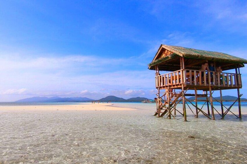 A wooden beach hut on stilts, clear shallow waters, and distant mountains. 2