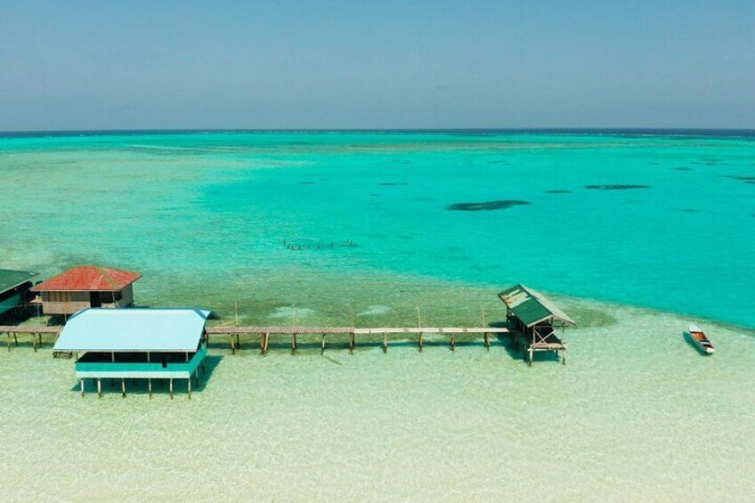 A beach with clear turquoise water, a wooden pier, and overwater bungalows. 4