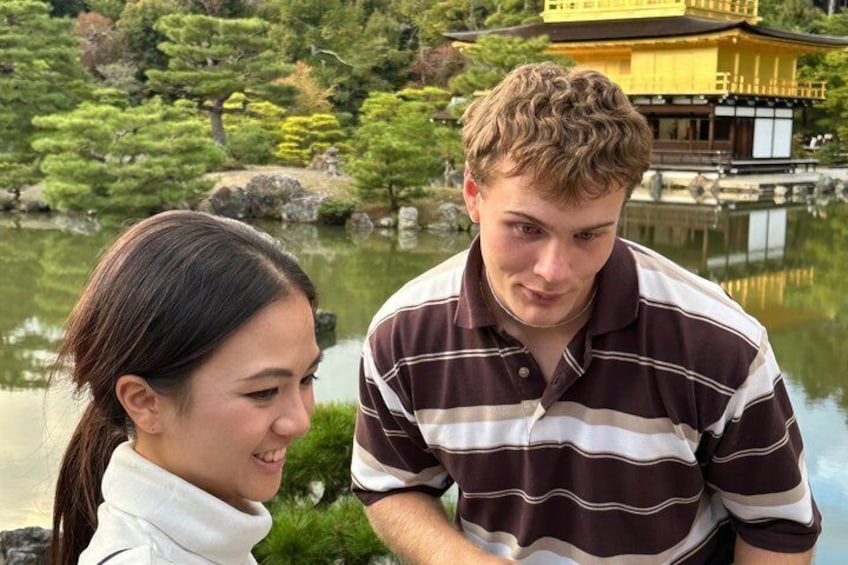 A man and a woman in a striped shirt and a white jacket, respectively, standing by a pond with a traditional building in the background. 5